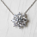 A silver snowflake pendant necklace with clear round-cut zirconia, displayed on a textured white background.