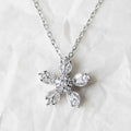 A silver-tone chain necklace with a five-petal flower pendant made of clear marquise-cut, displayed on a textured white background.